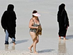 A western woman at a Dubai beach surrounded by women in traditional garb.