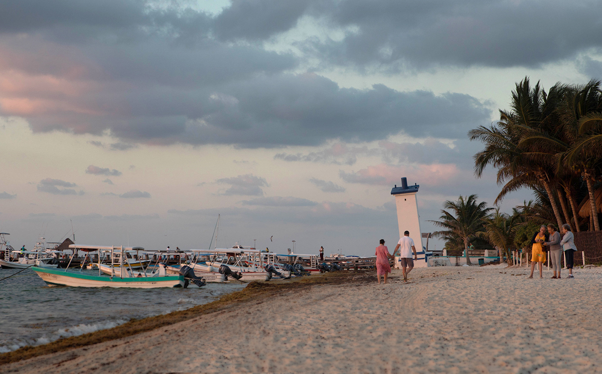 Early morning photo showing a couple walking on the beach toward the leaning lighthouse in Puerto Morelos, Mexico.