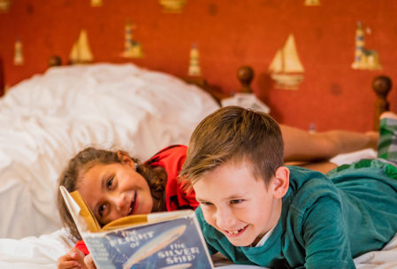 Two kids read a classic kids book while lounging on the bed in Ralphie's room at A Christmas Story House in Cleveland's Tremont neighborhood.